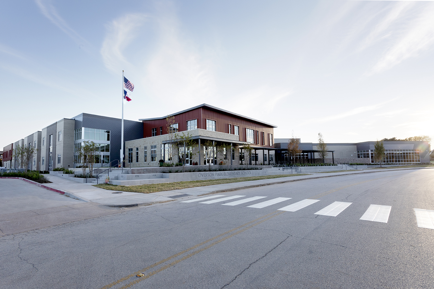 Street-view of a red and white elementary school with glass building and an American and Texas flag out front.